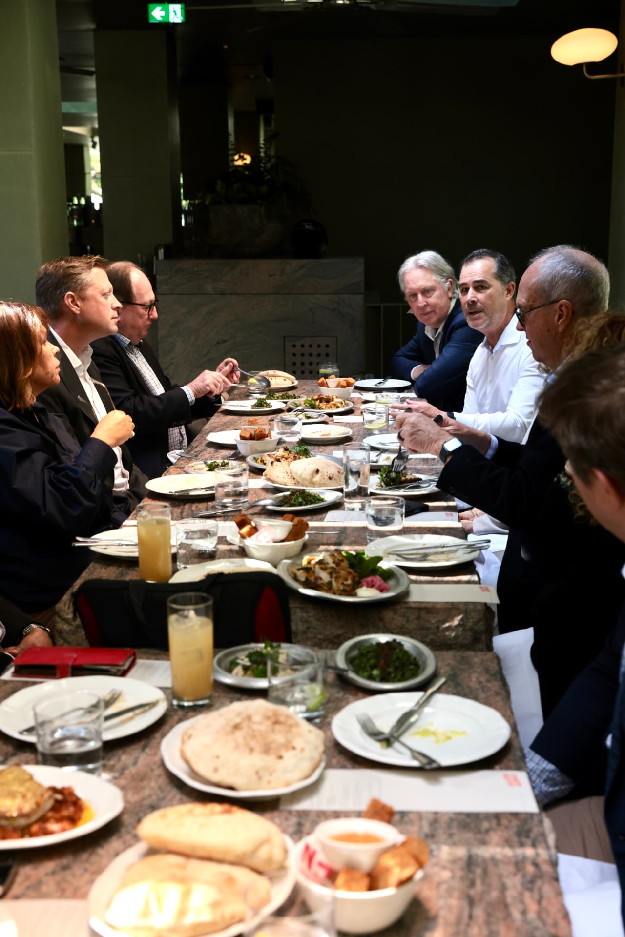 The long table mid-meal, shared dishes down the centre and conversation on both sides